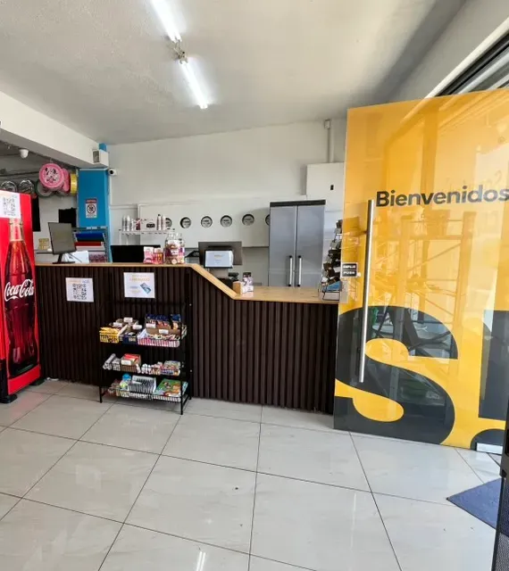 Entrada de la tienda: un panel de marca Bienvenidos junto al mostrador de caja, la registradora y la caja chica.