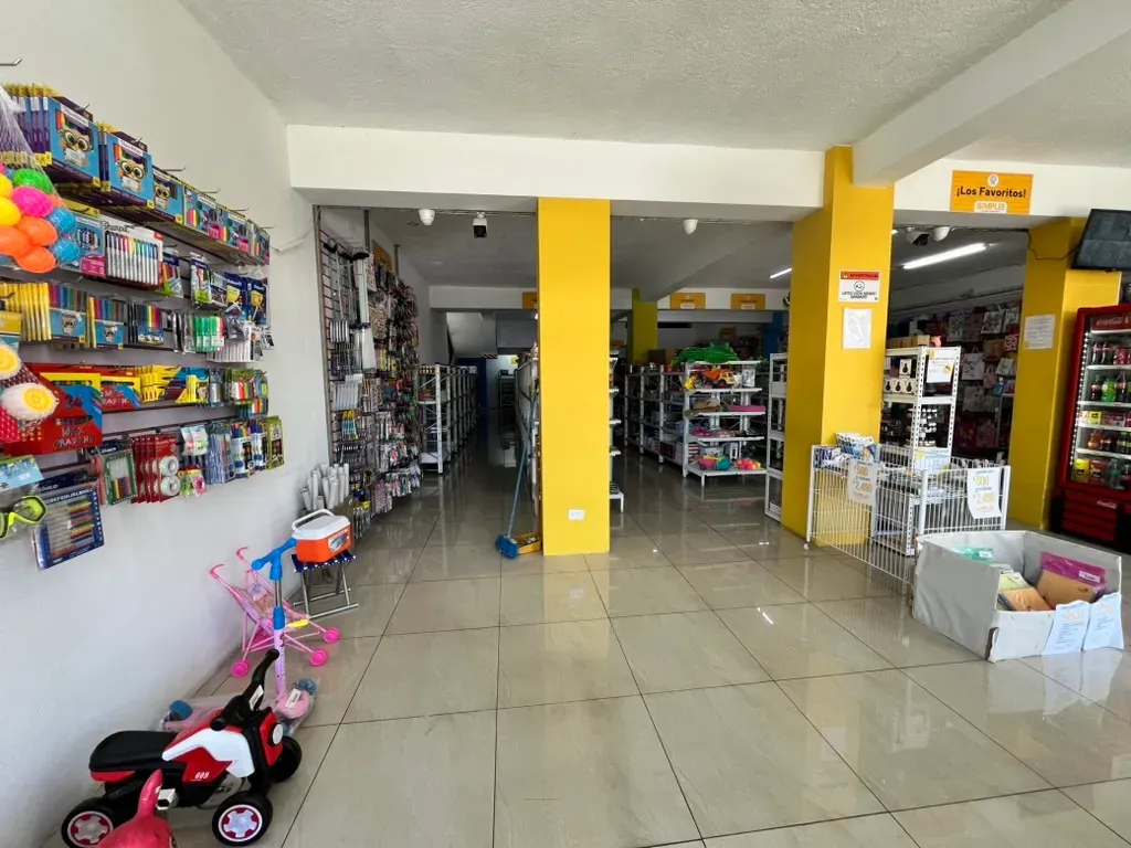 Un pasillo interior de la tienda con papelería y artículos para el hogar, que lleva hacia el departamento de juguetes.